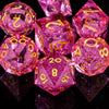 A collection of pink and purple polyhedral dice resting on a reflective black surface.