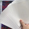 A stack of white double-sided diamond painting release paper is shown being held by a hand.