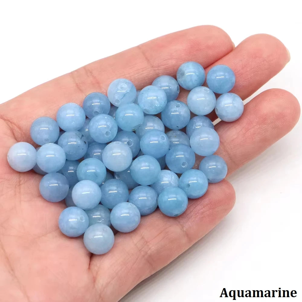 A hand holds a cluster of light blue aquamarine round beads for jewelry making.