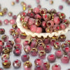 A pile of vibrant round beads in shades of pink and gold are scattered on a white surface.