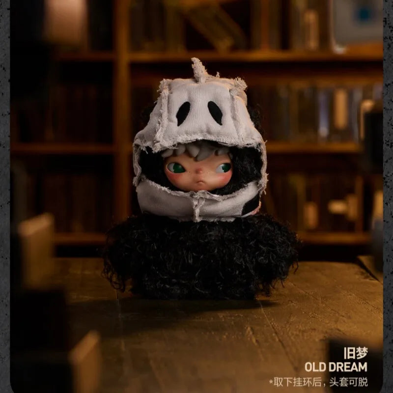 A small plush doll with a white mask and dark hair is displayed on a wooden surface.