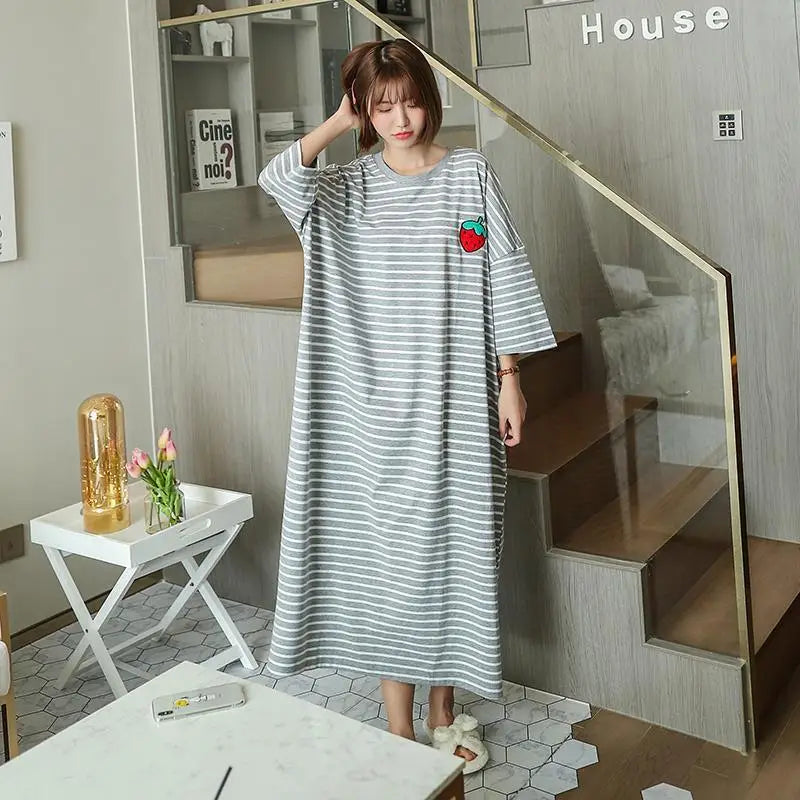 A woman models a long, gray and white striped short-sleeve lounge dress in a modern interior setting.