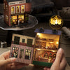 A hand holds a DIY wooden dollhouse kit featuring a pink princess villa with illuminated LED lights.