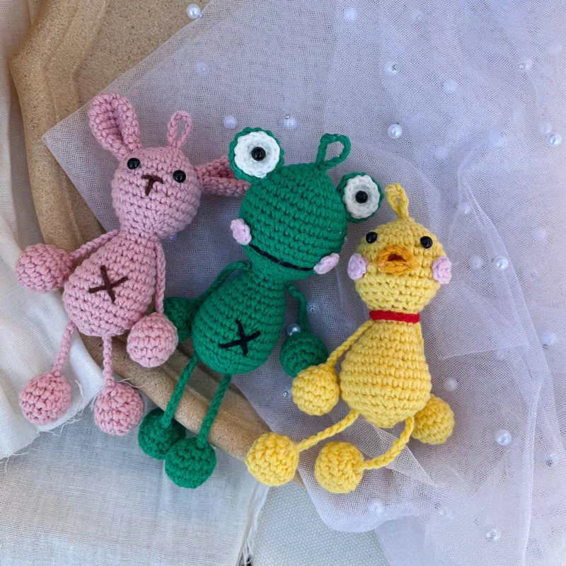 Handmade crochet frog hanging ornament in pink, green, and yellow yarn on sheer fabric