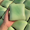 A hand holds a soft, light green squishy cube stress relief toy against a background of similar cubes.