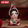 A collectible figure blind box of a girl with pink hair and large blue eyes sitting on a wooden surface.