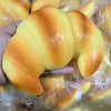 A golden croissant is visible inside a clear plastic bag, being held by a hand.