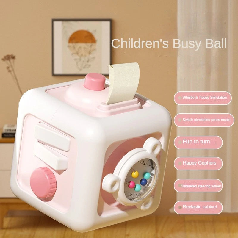 A pink and white children's busy ball cube featuring various sensory elements like a whistle, music, goppers, and a steering 