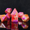 A collection of seven polyhedral dice featuring a vibrant pink and orange swirl pattern on a dark background.