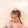 A young girl holds two realistic soft vinyl baby dolls with pink outfits against a light background.