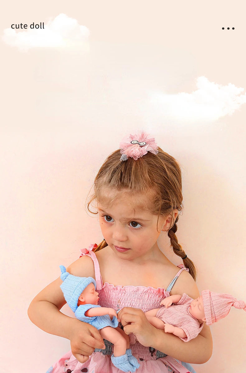 A young girl holds two realistic soft vinyl baby dolls with pink outfits against a light background.