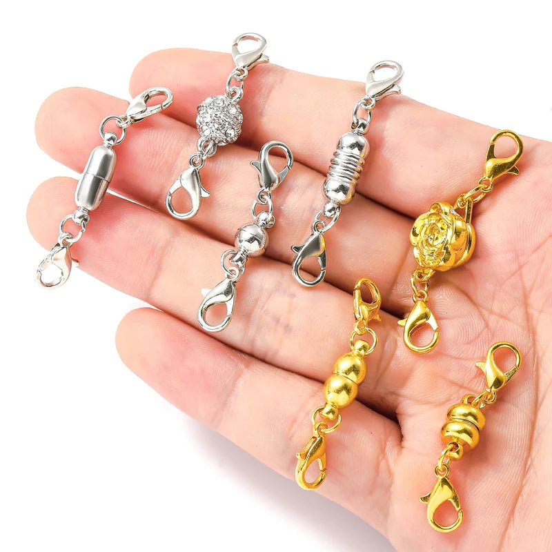 A hand holds a set of five magnetic lobster claw clasps for jewelry making, featuring silver and gold finishes.