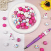 A collection of 25 silicone beads in various pink and white colors are displayed on a white plate and scattered around.