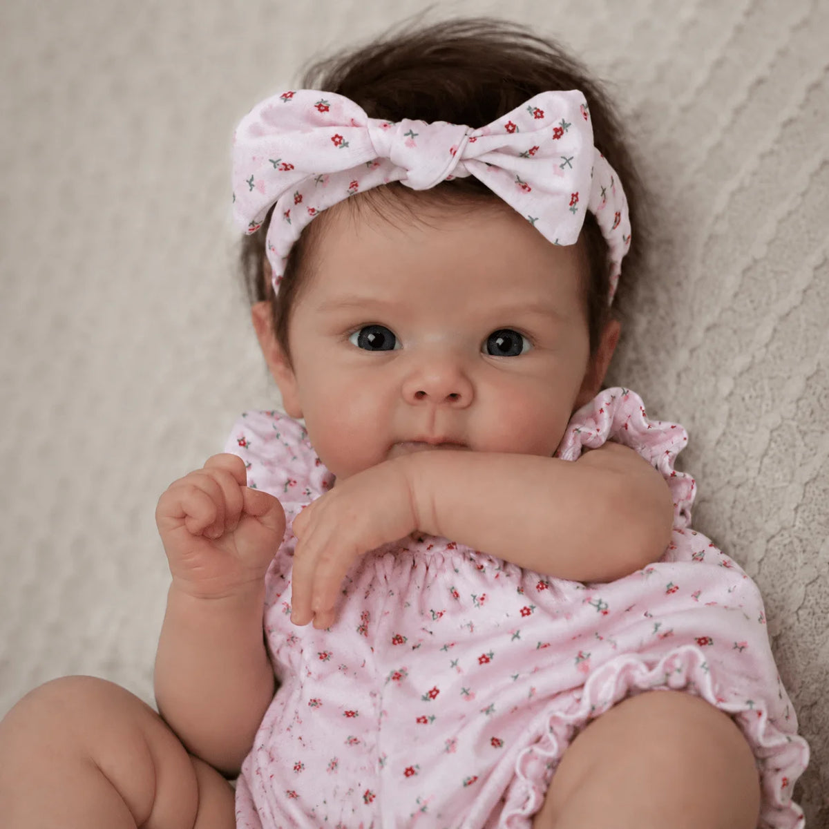 A close-up photo of a baby doll with hand-rooted hair wearing a pink floral outfit and a matching bow.