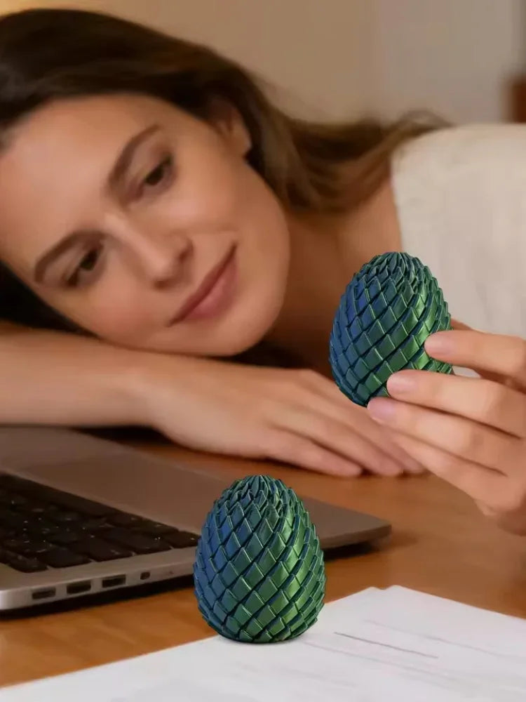 A woman is holding a teal dragon egg fidget spinner next to a laptop and some papers.