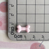 A small pink resin bone charm is placed on a ruler marked in centimeters and inches.