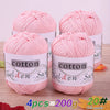 Four pink cotton knitting yarns in tubes are displayed on a wooden surface.