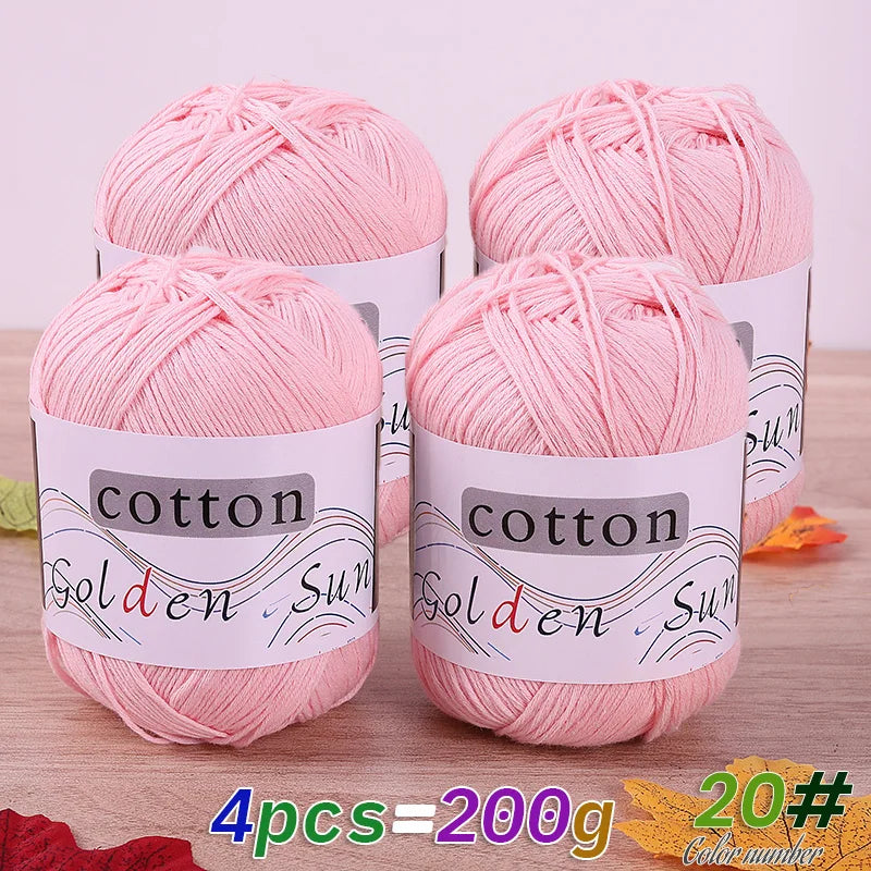 Four pink cotton knitting yarns in tubes are displayed on a wooden surface.