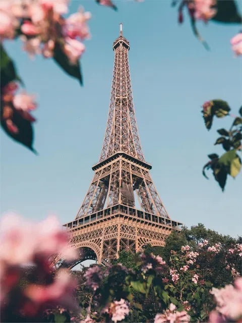 A close-up view of the Eiffel Tower against a blue sky, framed by pink flowers and green foliage.