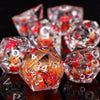 A close-up of a set of translucent resin dice with an orange and red floral pattern, reflecting on a dark surface.