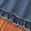 A close-up of a navy blue denim dress with a ruffled lace trim on the hem, laid on a wooden surface.