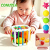A baby is interacting with a white plastic toy box filled with colorful, round, and shaped objects for sorting and play.