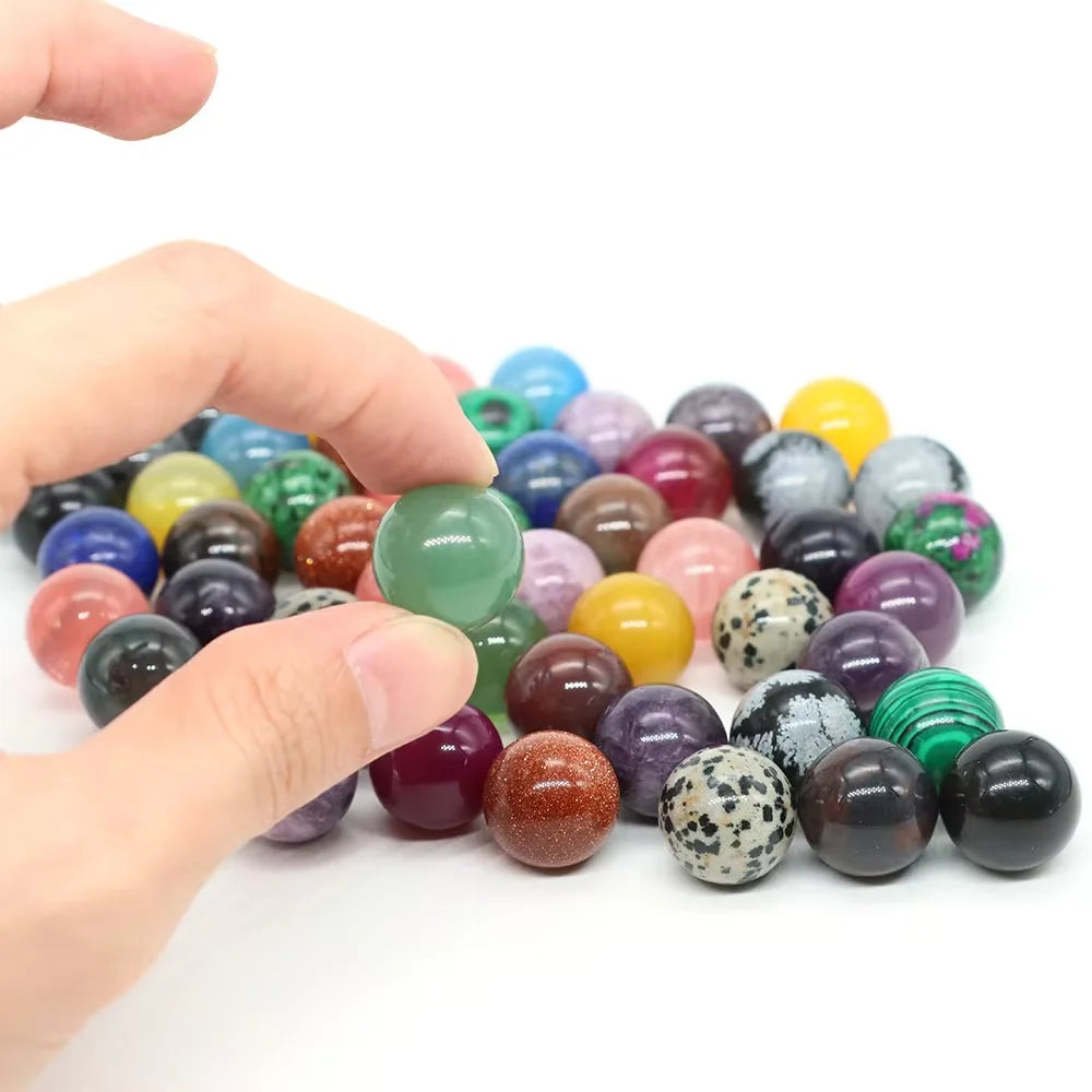 A hand is holding and displaying a collection of polished crystal spheres in various shades of green, purple, yellow, and bro