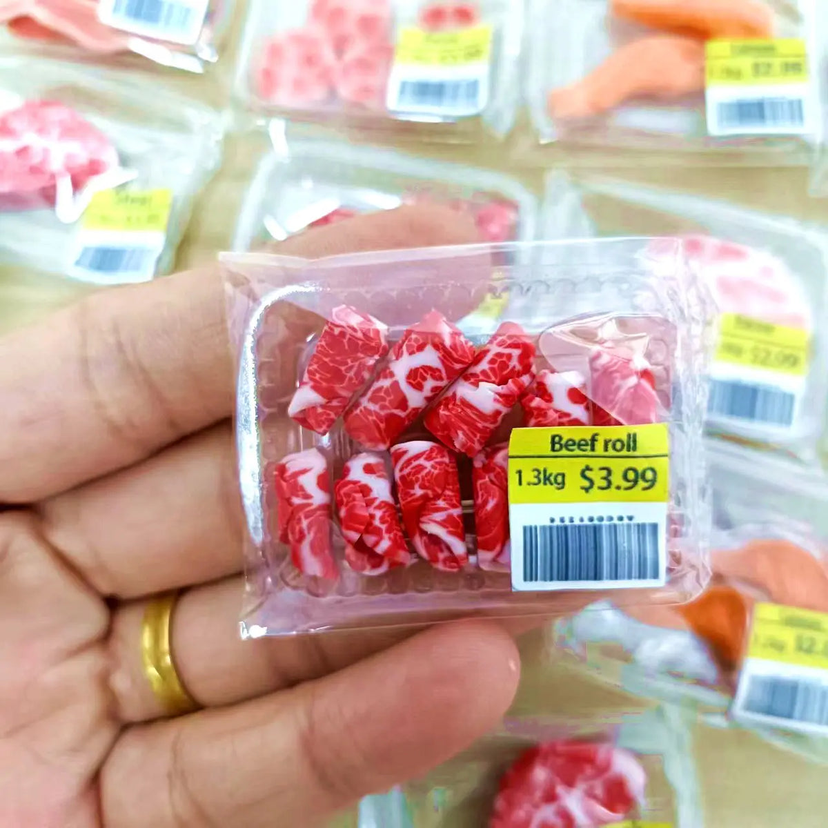 A hand holds a clear plastic package of beef rolls with a barcode, labeled 1.3kg for $3.99.