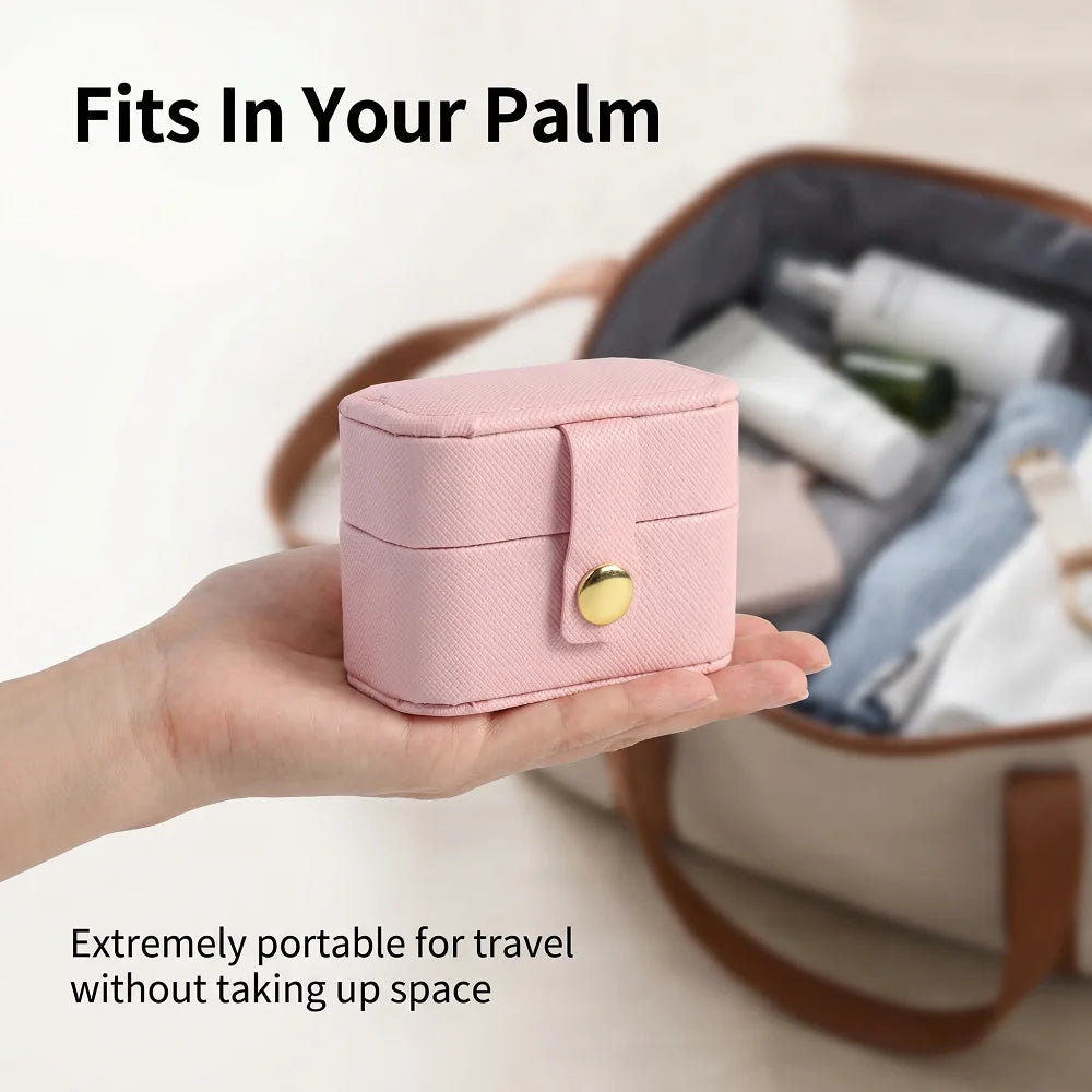 A pink portable leather jewelry storage box fits in a hand, shown next to travel toiletries.