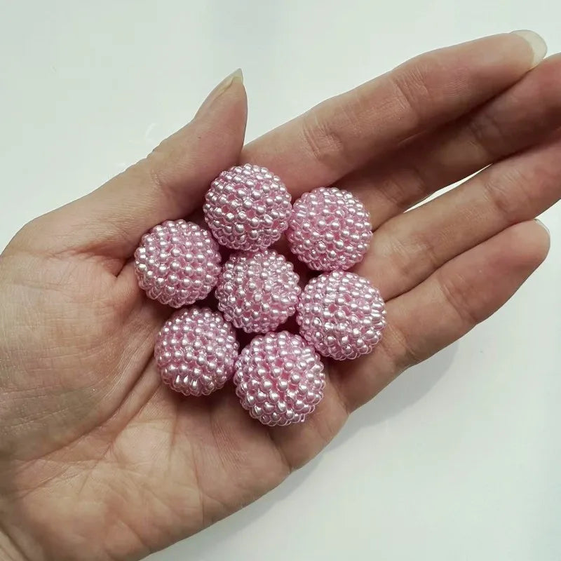 A hand holds a cluster of pink acrylic pearl beads for jewelry making