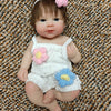 A realistic soft silicone reborn doll with brown hair and pink floral accessories sitting on a textured brown surface.
