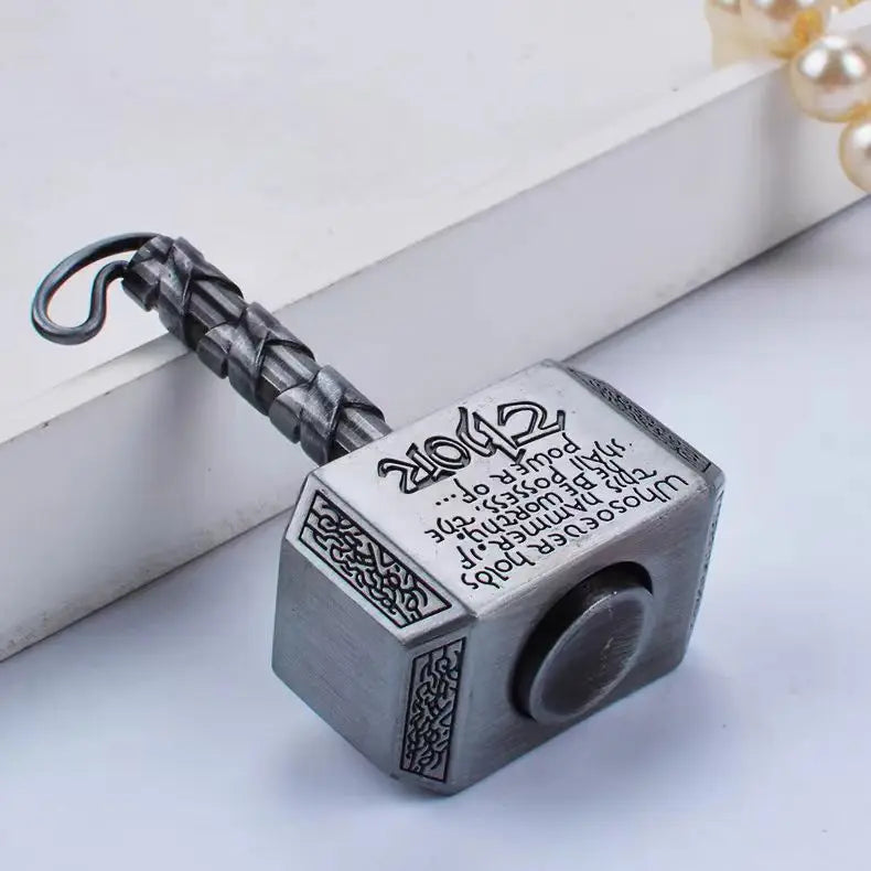 A silver hammer-shaped metal fidget spinner with a textured handle and a round top is shown on a white surface.