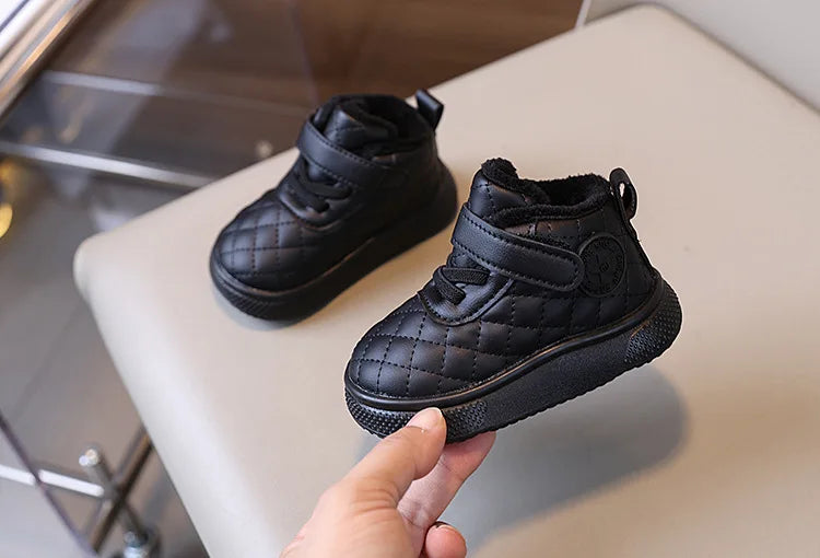 A hand holds a black quilted toddler winter snow boot with a soft sole and Velcro closure.
