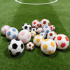 A collection of colorful, soft plush soccer balls scattered on a green artificial turf field.