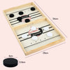 A wooden catapult tabletop hockey game board with black and white pucks and a winner marker.