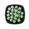 A black bowl filled with small, round, printed silicone beads in shades of green and brown featuring leopard and daisy patter