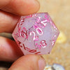A hand holds a pink hexagonal resin polyhedral die featuring pink floral designs and the number 2023.