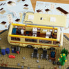 A building block set depicting a yellow RV camper bus with various accessories and a separate structure on a tan baseplate.