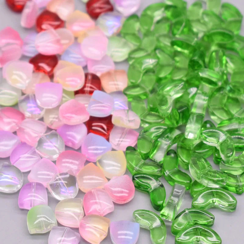 A collection of pink and green glass beads, including tulip flower shapes, scattered on a white surface.