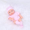 A realistic soft vinyl reborn baby doll wearing a pink outfit and hat, lying on white fluffy material.