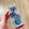 A hand holds a clear bottle filled with blue liquid and several translucent blue spheres, labeled Chiboki drink cup toy.