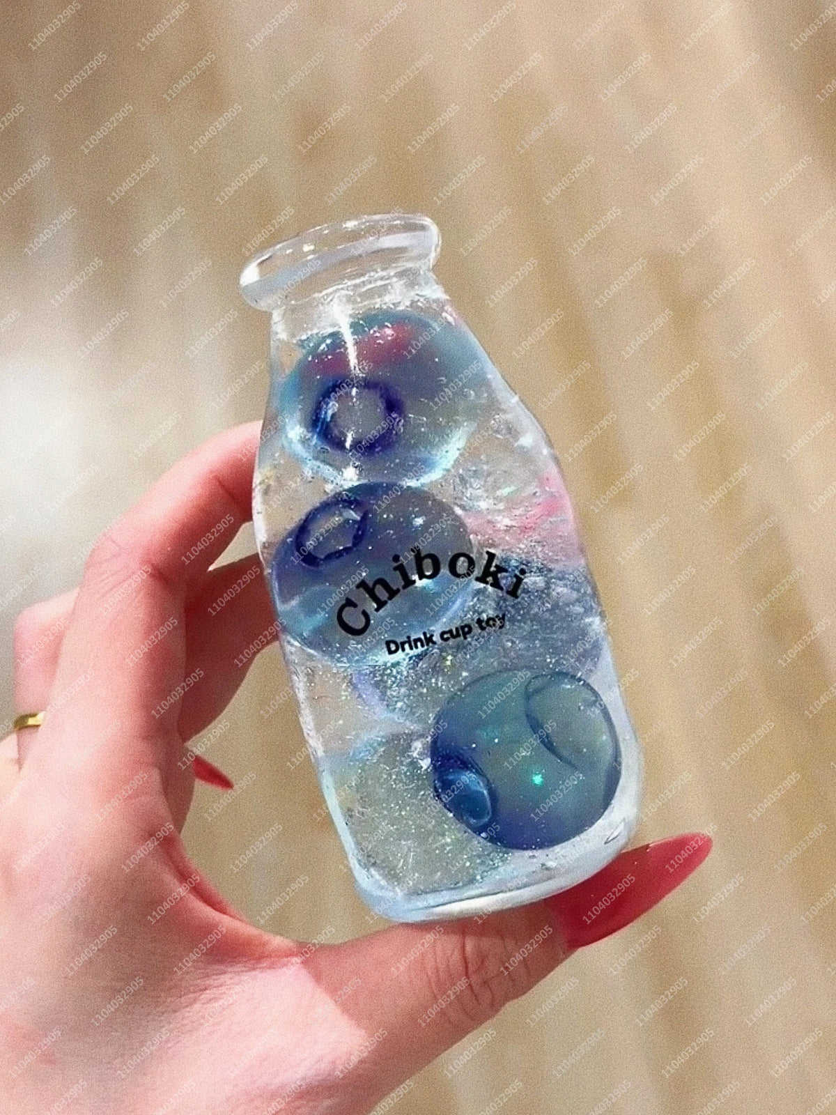 A hand holds a clear bottle filled with blue liquid and several translucent blue spheres, labeled Chiboki drink cup toy.