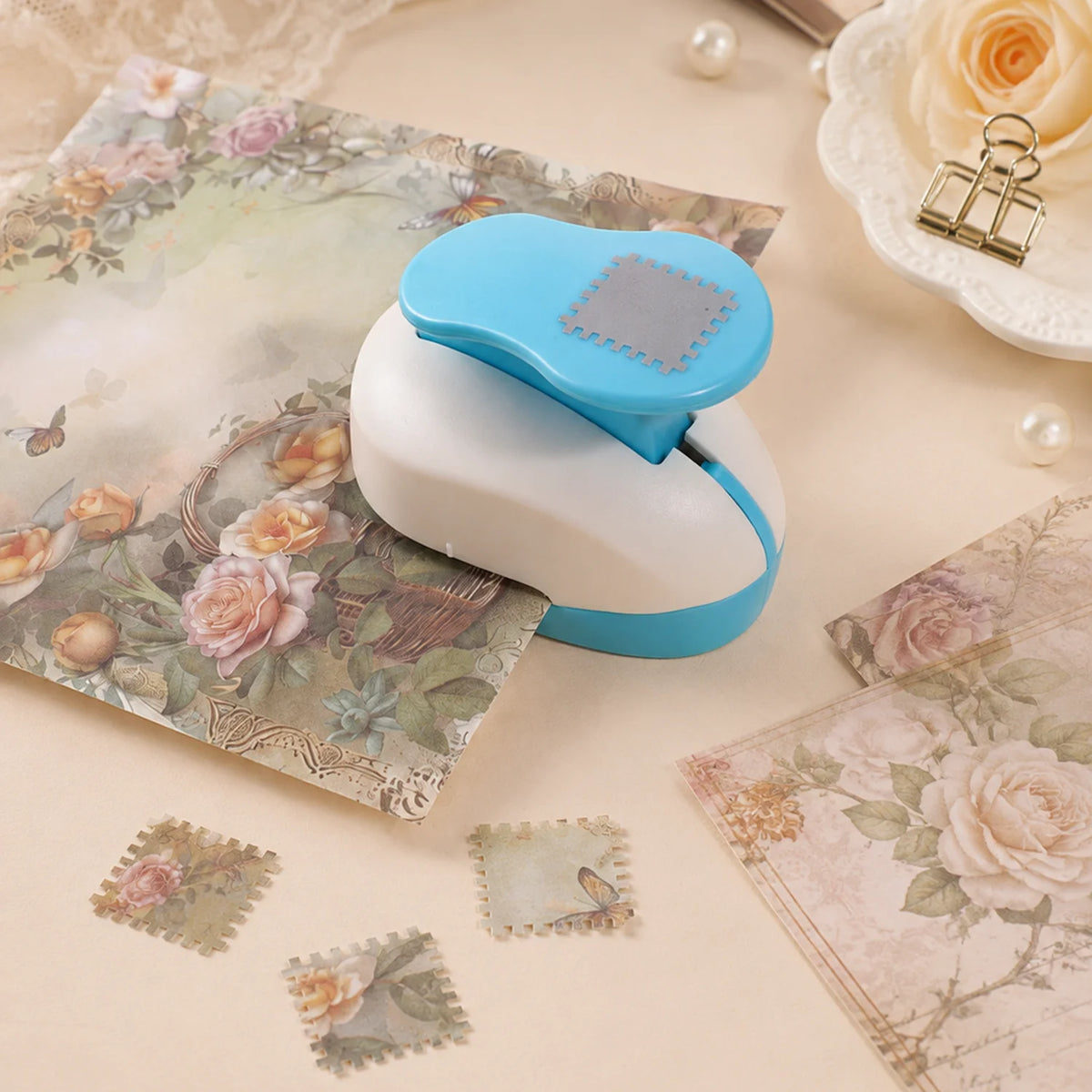 A light blue and white decorative square stamp edge paper is shown next to a white and blue stamp tool on a beige surface.