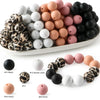 A collection of soft food-grade silicone beads in various colors including black, white, pink, and peach.