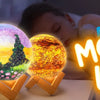 A close-up of a DIY Moon Lamp painting kit featuring three glowing spherical night lights resting on a wooden surface.