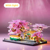 A miniature pink sakura tree building block set illuminated with lights on a dark base.