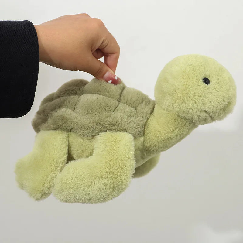 A soft, light green and olive colored simulated turtle plush doll being held by a hand.