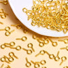 A pile of gold-colored metal eye pins and jump rings scattered on a white dish.
