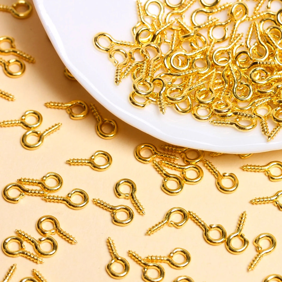 A pile of gold-colored metal eye pins and jump rings scattered on a white dish.