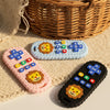 A lion-shaped silicone baby teether with remote control design is shown resting on a beige woven fabric next to a wicker bask